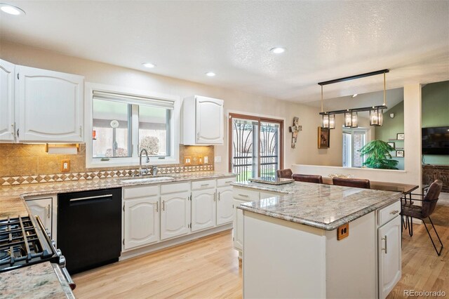 kitchen featuring light wood finished floors, backsplash, a kitchen island, black dishwasher, and a sink