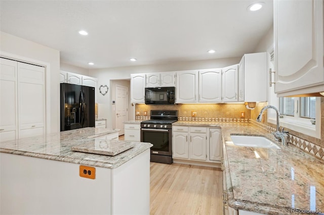 kitchen with black appliances, a sink, light stone counters, light wood-style floors, and decorative backsplash