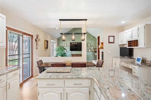 kitchen featuring light stone counters, hanging light fixtures, vaulted ceiling, white cabinetry, and light wood-type flooring