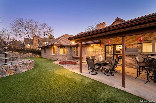 rear view of house with brick siding, a chimney, a lawn, and a patio area