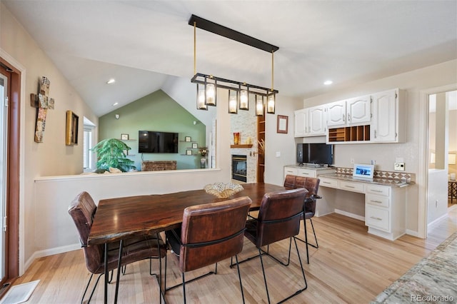 dining area featuring visible vents, a stone fireplace, light wood finished floors, lofted ceiling, and built in study area