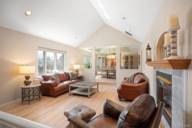 living area featuring wood finished floors, visible vents, baseboards, high vaulted ceiling, and a tile fireplace