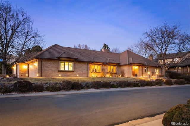 view of front facade featuring a tile roof, an attached garage, brick siding, and a chimney