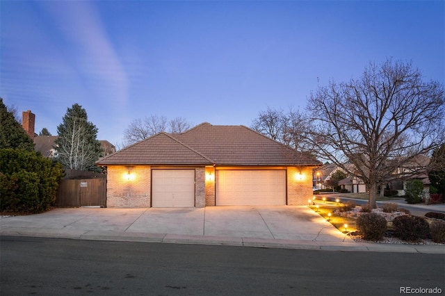 view of front of home with driveway, a tile roof, fence, an attached garage, and brick siding