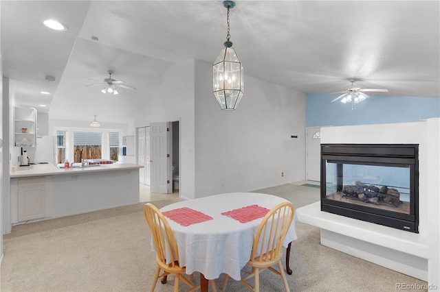 dining area featuring a multi sided fireplace, light carpet, a ceiling fan, and vaulted ceiling