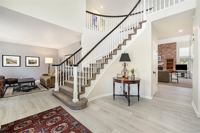 stairs with a high ceiling, hardwood / wood-style floors, and a brick fireplace