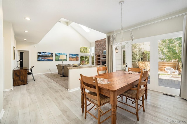 dining area featuring a skylight, high vaulted ceiling, and light hardwood / wood-style flooring