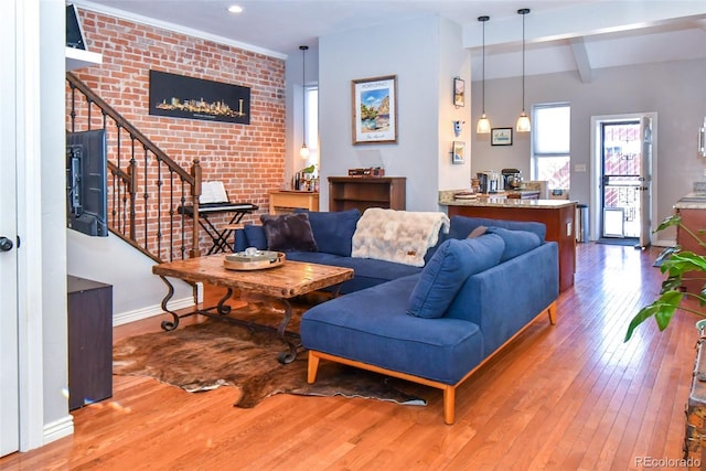 living room with stairway, hardwood / wood-style floors, brick wall, beamed ceiling, and baseboards