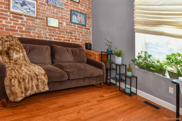 interior space featuring brick wall, visible vents, baseboards, and wood finished floors