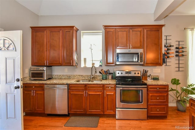 kitchen featuring stainless steel appliances, light wood-style floors, a sink, and light stone countertops