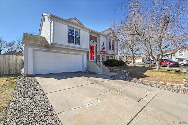 raised ranch with a garage, fence, and concrete driveway