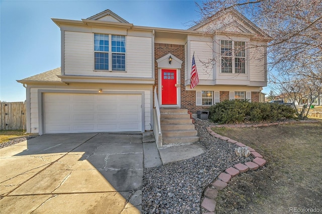 split foyer home featuring a garage, fence, concrete driveway, and brick siding