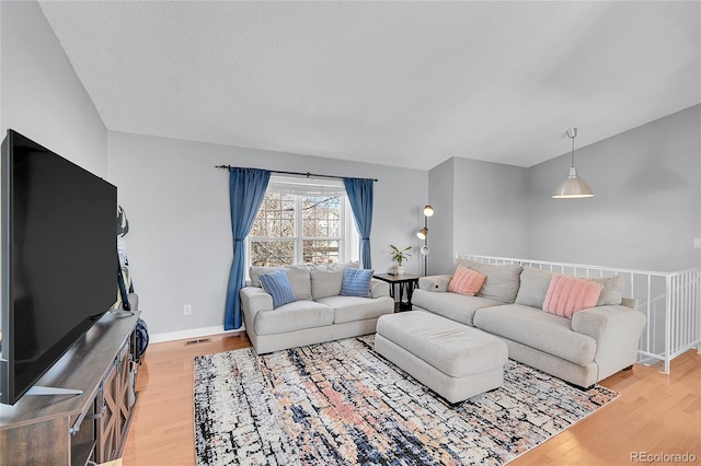 living area with a textured ceiling, light wood finished floors, visible vents, and baseboards