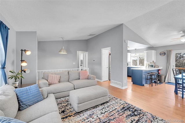 living room featuring lofted ceiling, light wood-style floors, visible vents, and a textured ceiling