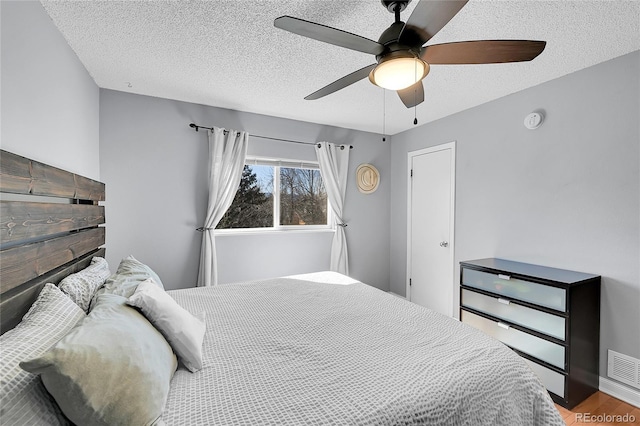 bedroom featuring visible vents, ceiling fan, a textured ceiling, wood finished floors, and baseboards