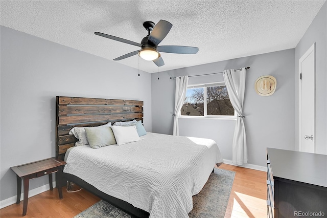 bedroom featuring ceiling fan, a textured ceiling, baseboards, and light wood-style floors