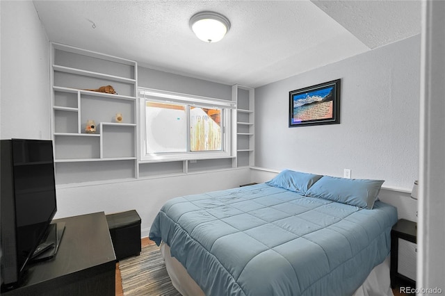 bedroom featuring a textured ceiling, a textured wall, and wood finished floors