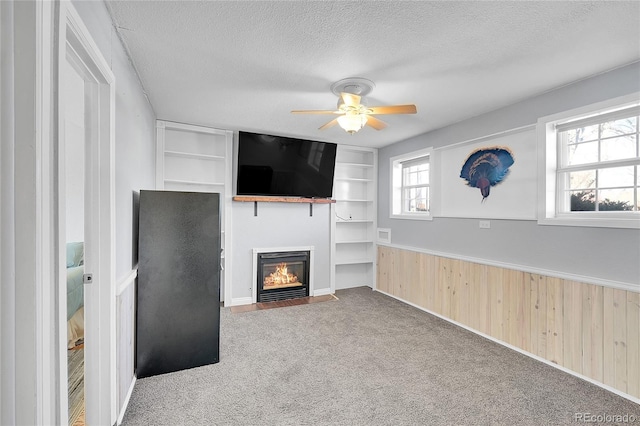 unfurnished living room with wainscoting, a fireplace with flush hearth, a textured ceiling, carpet floors, and built in shelves