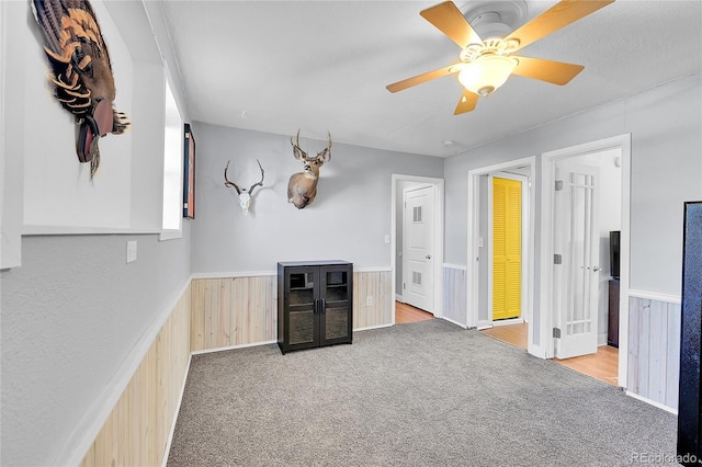 bar featuring a wainscoted wall, ceiling fan, carpet flooring, and wooden walls