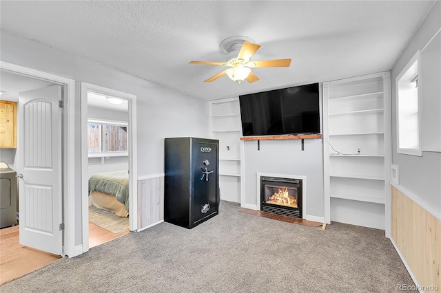 carpeted living room with a ceiling fan, a wainscoted wall, a fireplace with flush hearth, washer / clothes dryer, and a textured ceiling