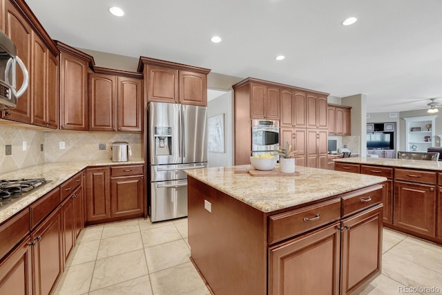kitchen featuring a kitchen island, backsplash, appliances with stainless steel finishes, and light stone counters