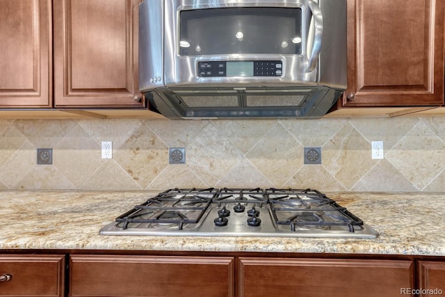 kitchen featuring backsplash, brown cabinets, light stone countertops, and stainless steel gas stovetop