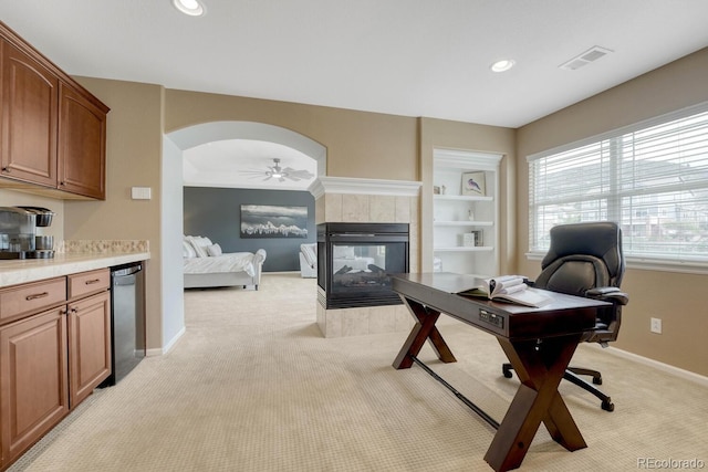 home office featuring a ceiling fan, visible vents, arched walkways, a fireplace, and light carpet