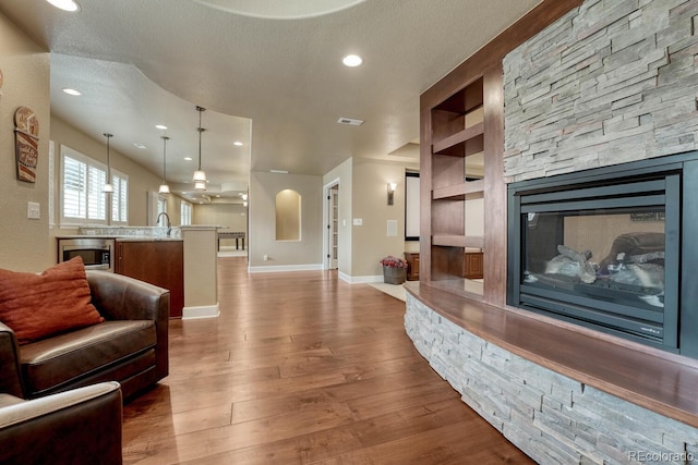 living room with a fireplace, recessed lighting, baseboards, wood finished floors, and visible vents