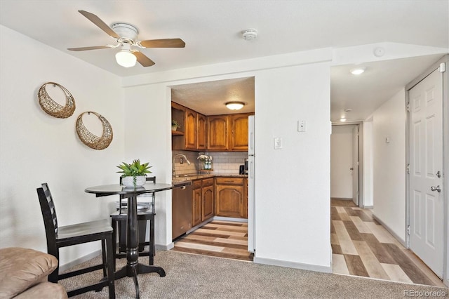 kitchen featuring a sink, tasteful backsplash, stainless steel dishwasher, brown cabinetry, and light wood finished floors