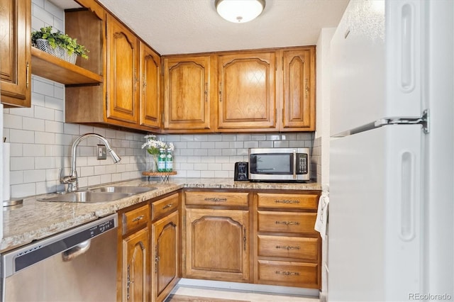 kitchen with brown cabinetry, open shelves, stainless steel appliances, and a sink