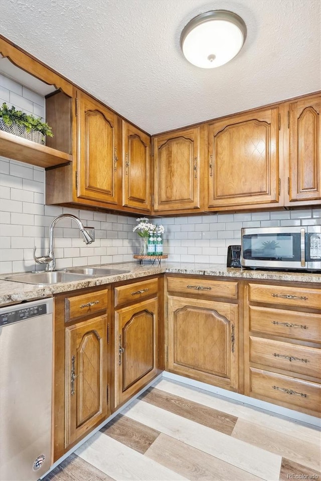 kitchen featuring tasteful backsplash, light wood-style floors, brown cabinetry, stainless steel appliances, and a sink