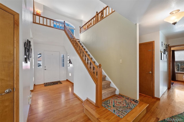 foyer featuring baseboards, light wood-style floors, a towering ceiling, and stairs