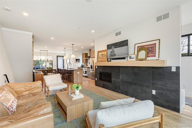 living room featuring light wood-type flooring, visible vents, a fireplace, and recessed lighting