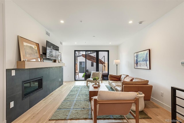 living area featuring light wood-type flooring, a tiled fireplace, visible vents, and recessed lighting