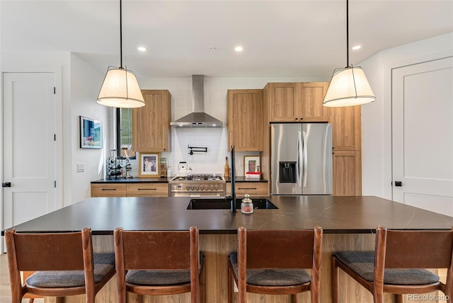 kitchen featuring dark countertops, wall chimney range hood, a sink, decorative backsplash, and stainless steel fridge