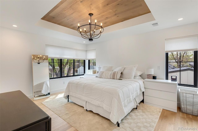 bedroom with light wood finished floors, a chandelier, visible vents, and a raised ceiling