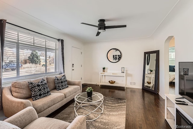 living room with baseboards, visible vents, arched walkways, ceiling fan, and dark wood-type flooring