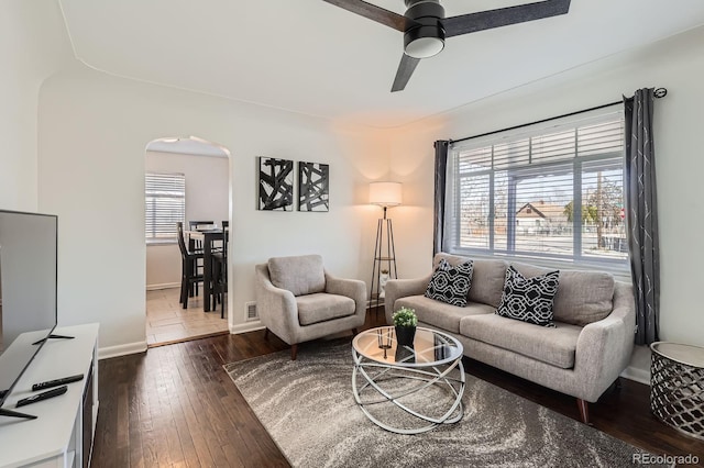 living area featuring a ceiling fan, visible vents, baseboards, dark wood finished floors, and arched walkways