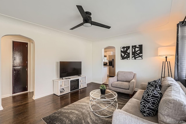 living area featuring a ceiling fan, arched walkways, dark wood-style flooring, and baseboards