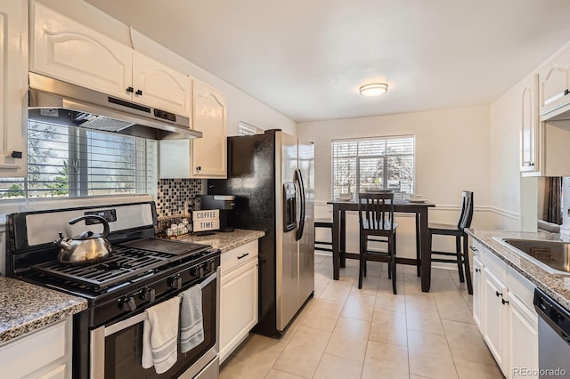 kitchen with under cabinet range hood, tasteful backsplash, stainless steel appliances, white cabinets, and light tile patterned floors