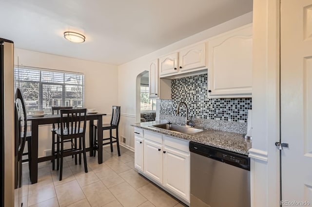 kitchen featuring tasteful backsplash, dishwasher, freestanding refrigerator, arched walkways, and a sink