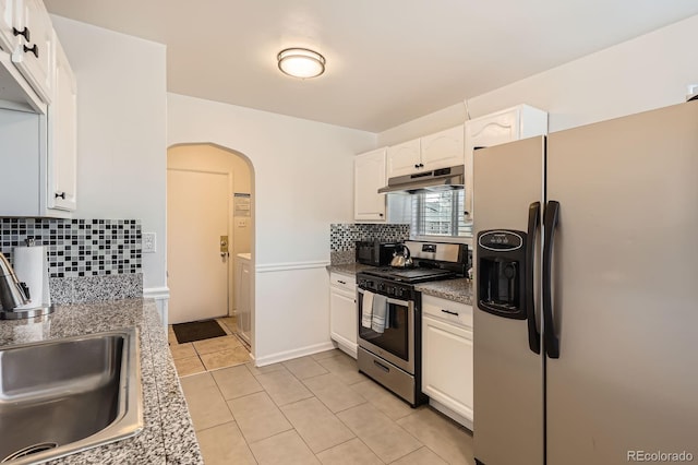 kitchen featuring under cabinet range hood, appliances with stainless steel finishes, arched walkways, white cabinetry, and a sink