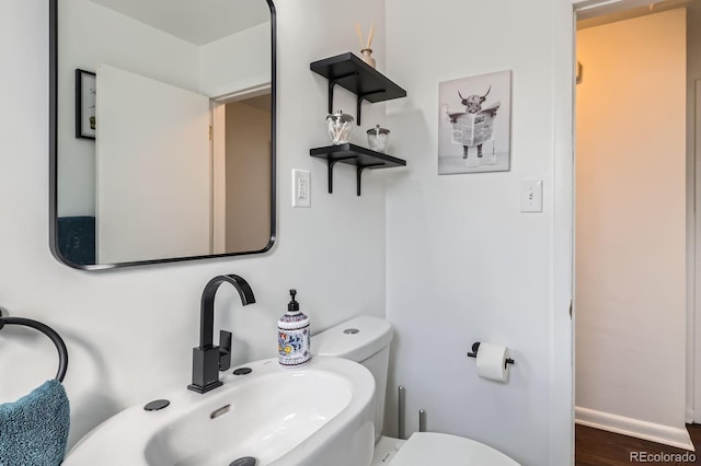 half bath with wood finished floors, toilet, baseboards, and a sink