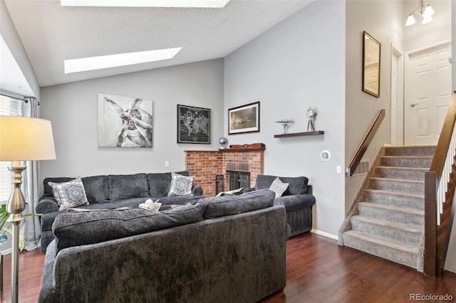 living room with a textured ceiling, a chandelier, a fireplace, dark hardwood / wood-style floors, and lofted ceiling with skylight