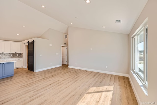 kitchen featuring lofted ceiling, light hardwood / wood-style flooring, white cabinetry, a barn door, and decorative backsplash