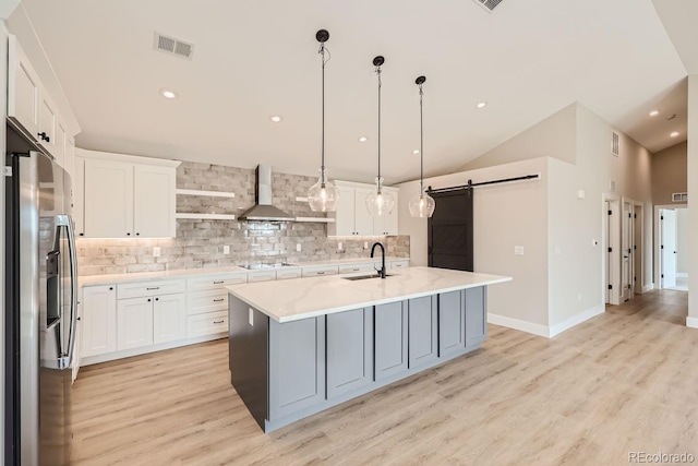 kitchen with a barn door, wall chimney exhaust hood, pendant lighting, white cabinets, and stainless steel refrigerator with ice dispenser