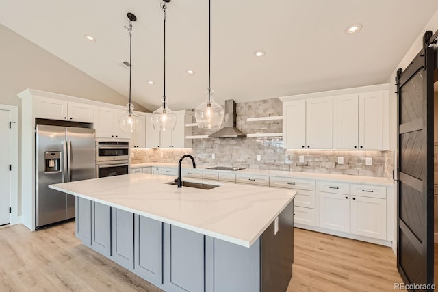 kitchen with stainless steel appliances, sink, hanging light fixtures, white cabinetry, and a barn door