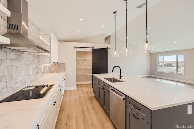 kitchen featuring white cabinets, lofted ceiling, stainless steel dishwasher, wall chimney exhaust hood, and a barn door