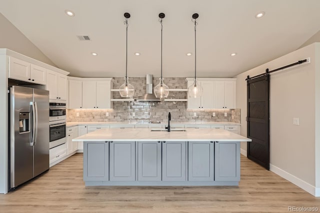 kitchen with a center island with sink, wall chimney range hood, white cabinetry, stainless steel appliances, and a barn door