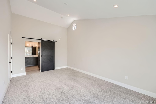 unfurnished bedroom with a barn door, light colored carpet, vaulted ceiling, and ensuite bath